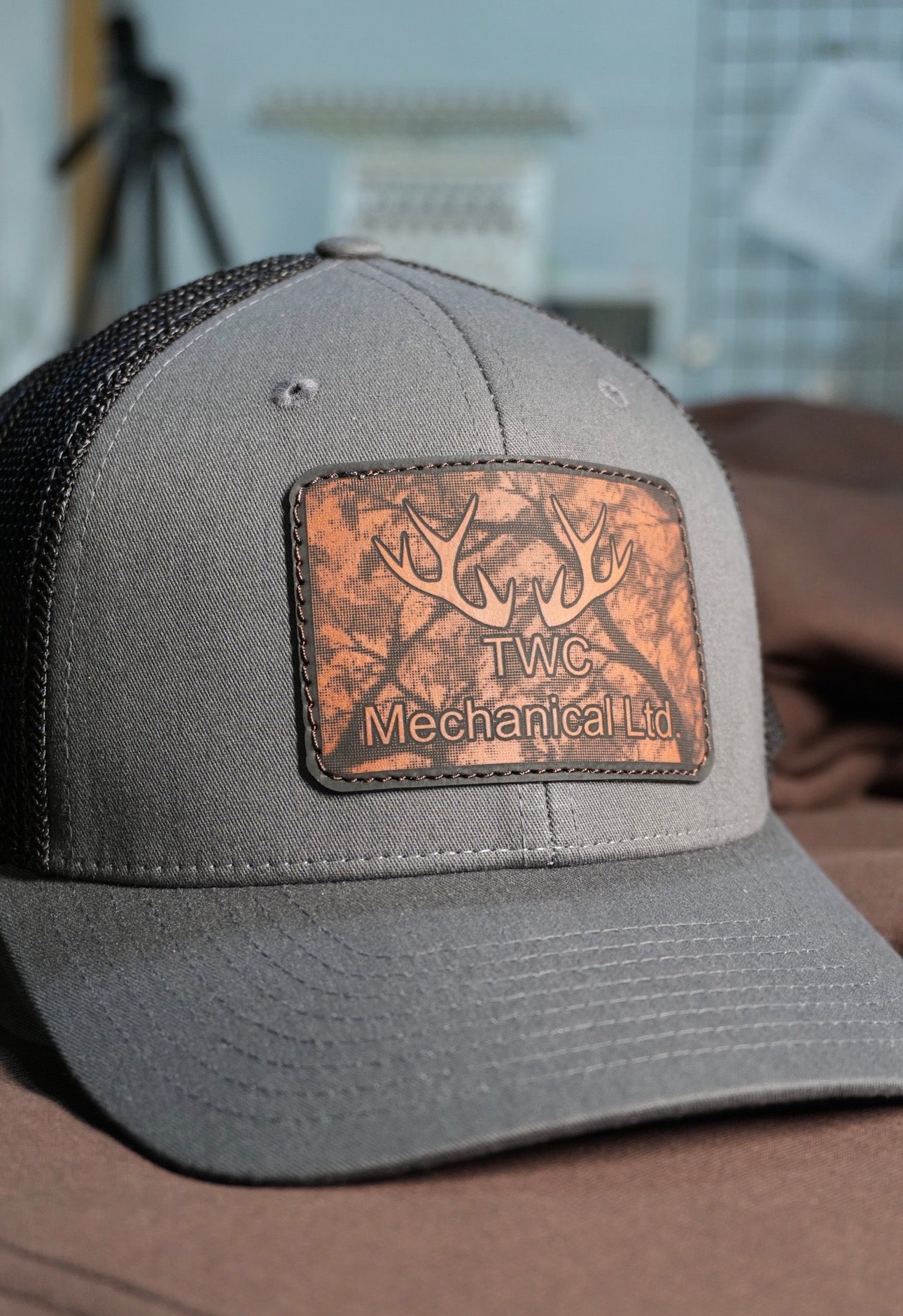 Gray cap with a leather patch featuring 'TWC Mechanical Ltd' on a blurred background